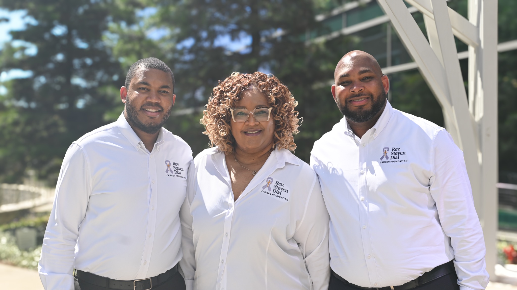Three people together outdoors wearing Rev. Steven Dial Cancer Foundation shirts.